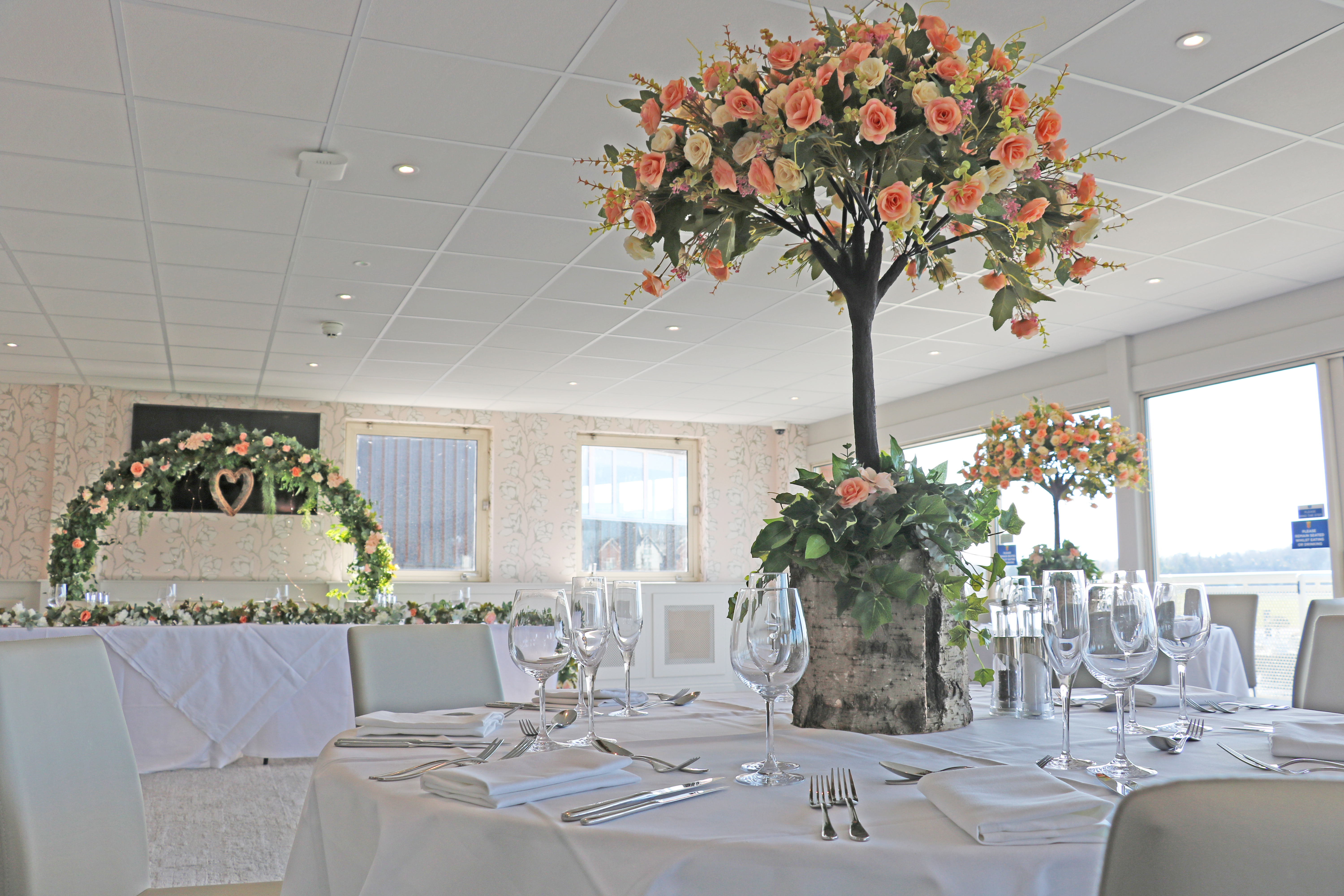 Leverhulme Chester Racecourse dressed for Wedding reception. Orange and pink floral decoration. Flower, botanic arch with heart decoration and table centrepiece 