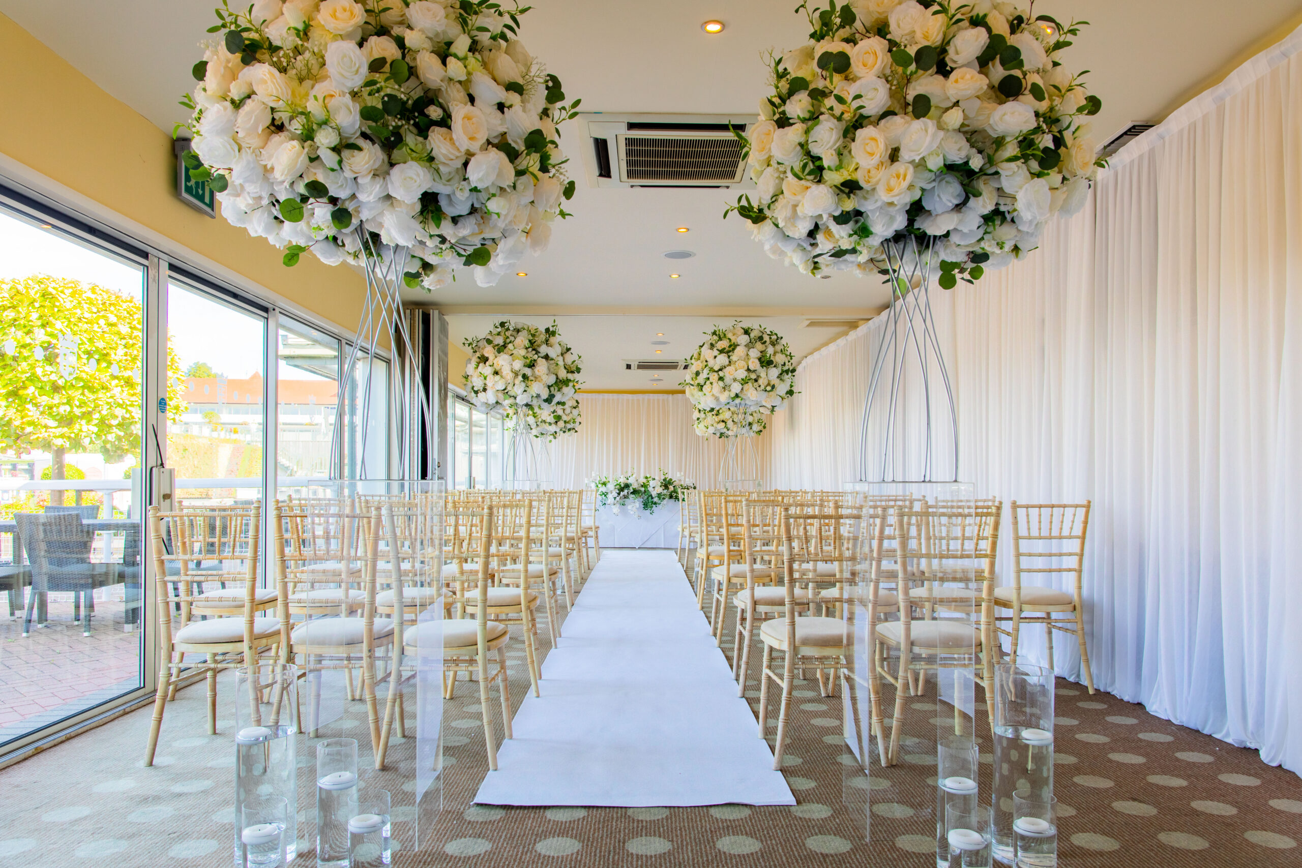 White and Yellow wedding decoration in the Paddock Rooms at Chester Racecourse. Wedding Ceremony aisle lined with white and yellow rose bushes. 